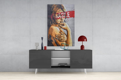 Glass wall art featuring portrait of young girl with brown hair and red censorship stripe, displayed above gray media console.