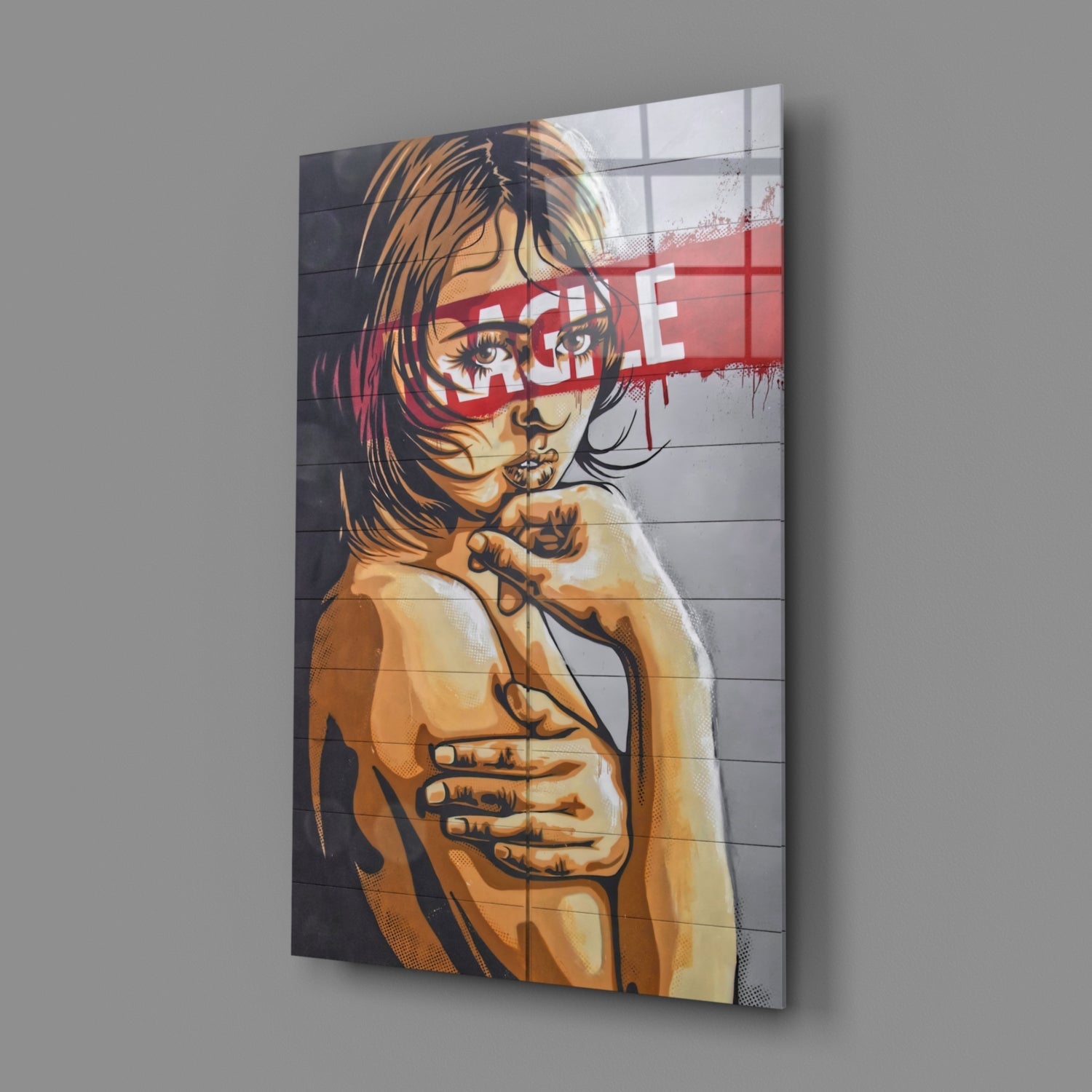 Angled view of glass wall art depicting a portrait illustration with orange and black tones, red text overlay, mounted on gray wall.