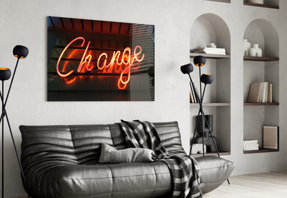 Orange neon "Change" text on glass wall art displayed above black leather sofa in modern living room interior.
