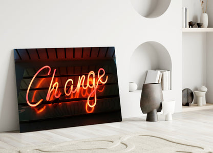 Neon "Change" glass wall art leaning against white wall in minimalist interior with shelving and decorative objects.