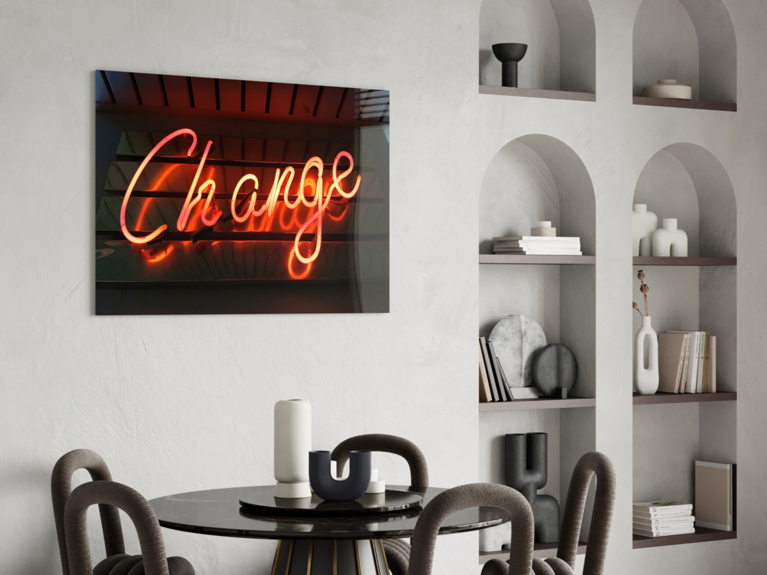 Neon "Change" sign in orange-red cursive glows above a round black dining table with gray upholstered chairs, beside white arched wall shelving.