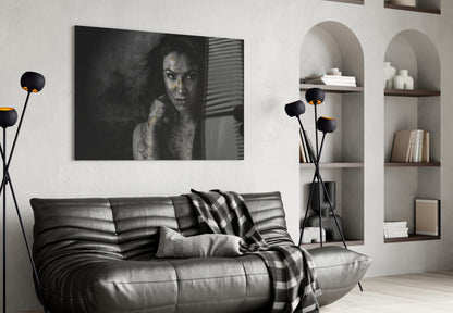 Black and white glass wall art of tattooed woman displayed above leather sofa in modern living room with shelving.