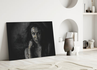 Black and white portrait of tattooed woman leaning against white wall in minimalist interior with shelving and decorative objects.