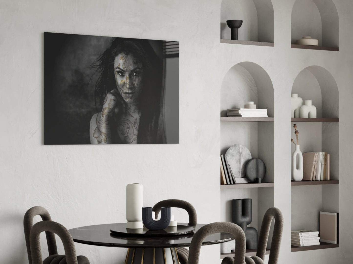 Black and white glass wall art of tattooed woman displayed above round dining table in modern interior setting.
