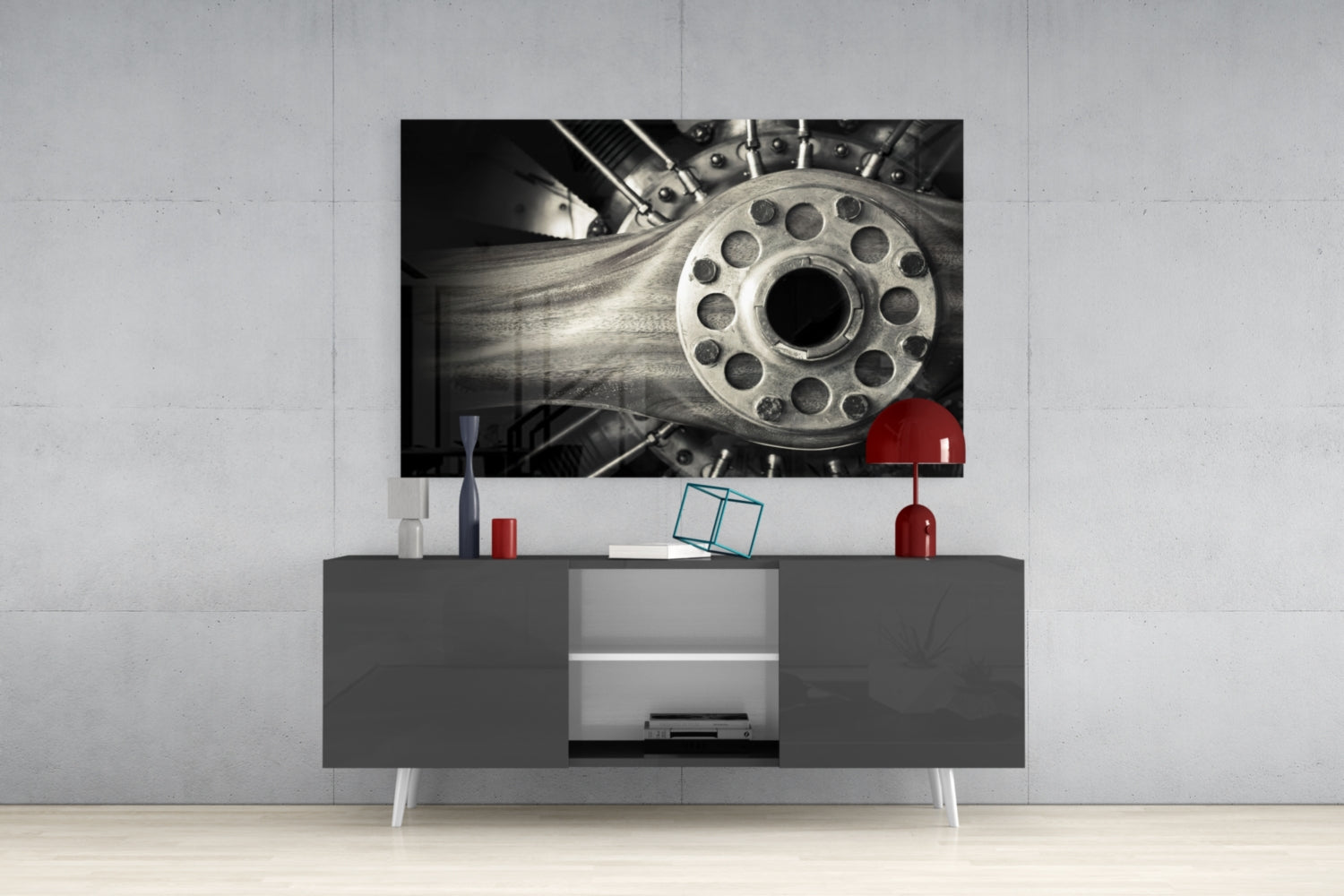 Black and white glass wall art featuring a detailed mechanical wheel mounted above a dark gray media console in a modern living room setting.