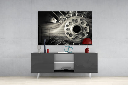 Black and white glass wall art featuring a detailed mechanical wheel mounted above a dark gray media console in a modern living room setting.