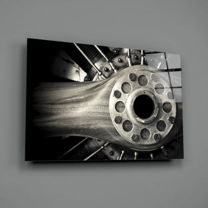 Close-up black and white photograph of a metal wheel hub with circular holes mounted on wood grain surface, displayed as wall art.