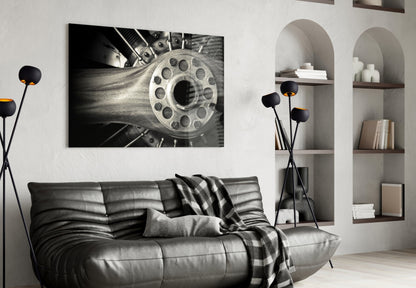 Black and white photograph of industrial wheel mechanism displayed as framed wall art above gray leather sofa in modern living room.