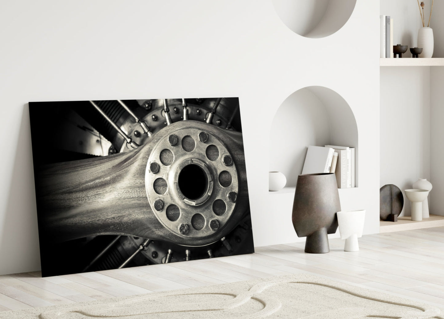 Black and white photograph of a motorcycle wheel with bolt pattern, leaning against white wall in minimalist interior setting.