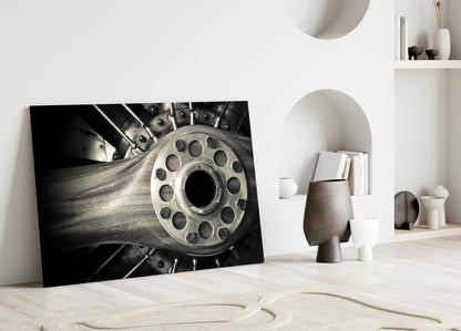 Black and white photograph of a motorcycle wheel with bolt pattern, leaning against white wall in minimalist interior setting.