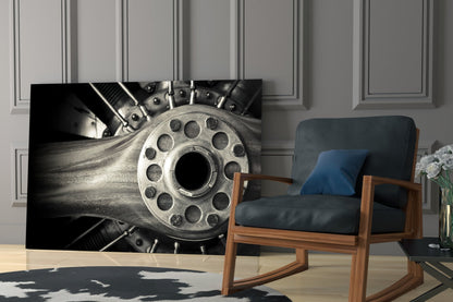 Black and white industrial wheel wall art displayed in modern living room beside wooden chair with blue cushions.