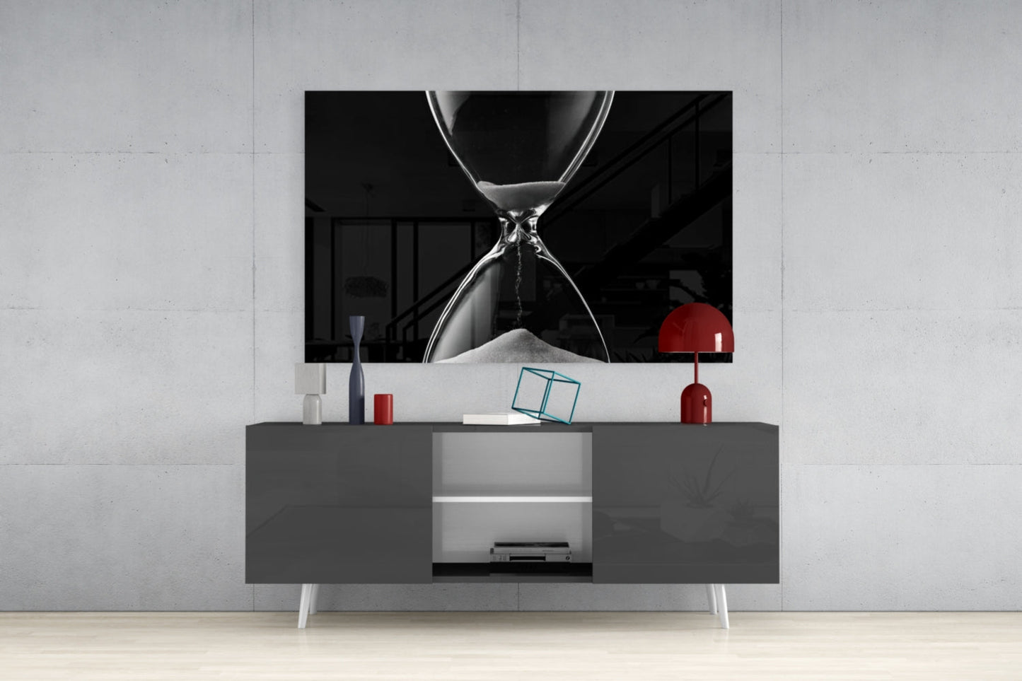 Black and white hourglass artwork displayed above gray media console with red decorative lamp and accessories in modern living room setting.