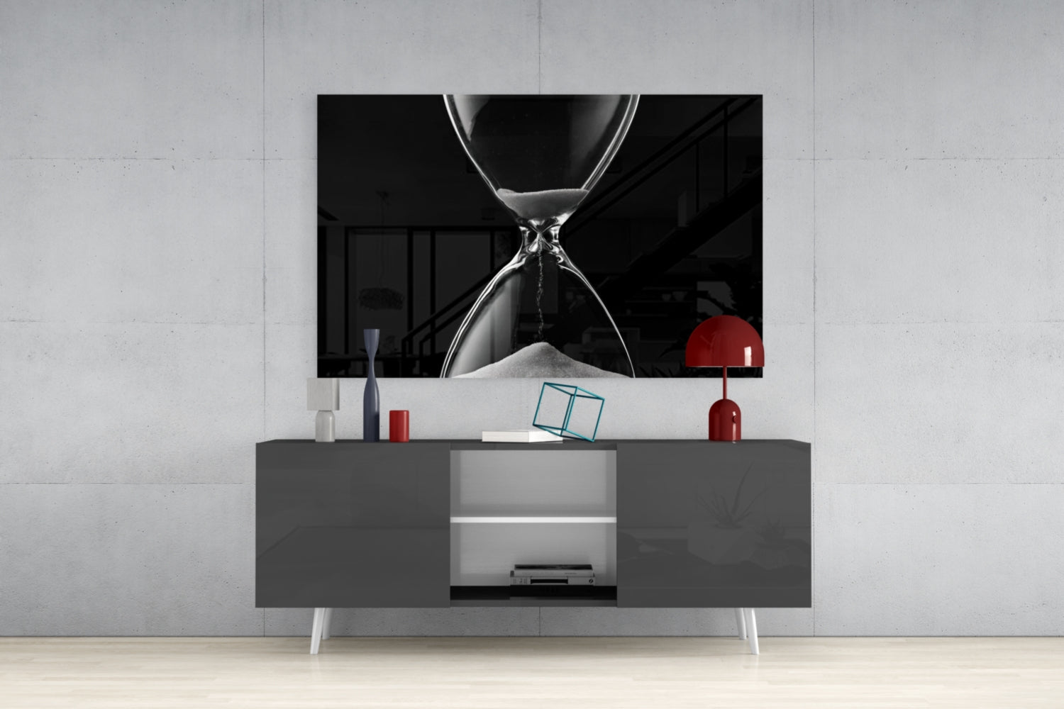 Black and white hourglass artwork displayed above gray media console with red decorative lamp and accessories in modern living room setting.