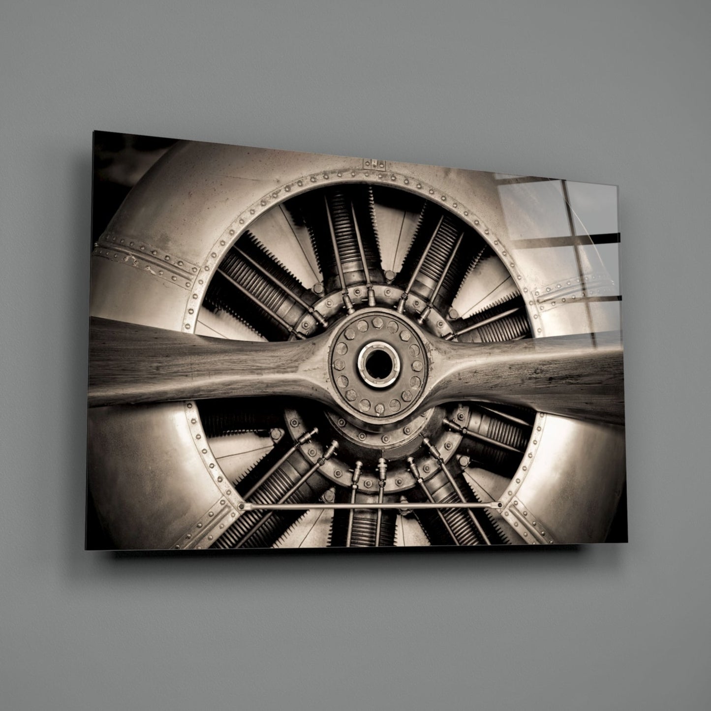Sepia-toned close-up of vintage aircraft radial engine with nine cylinders, wooden propeller, and riveted metal housing mounted on gray wall.
