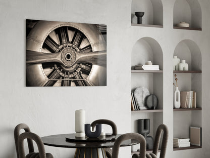 Sepia-toned aircraft propeller glass wall art displayed above a round black dining table in a modern interior with built-in shelving.
