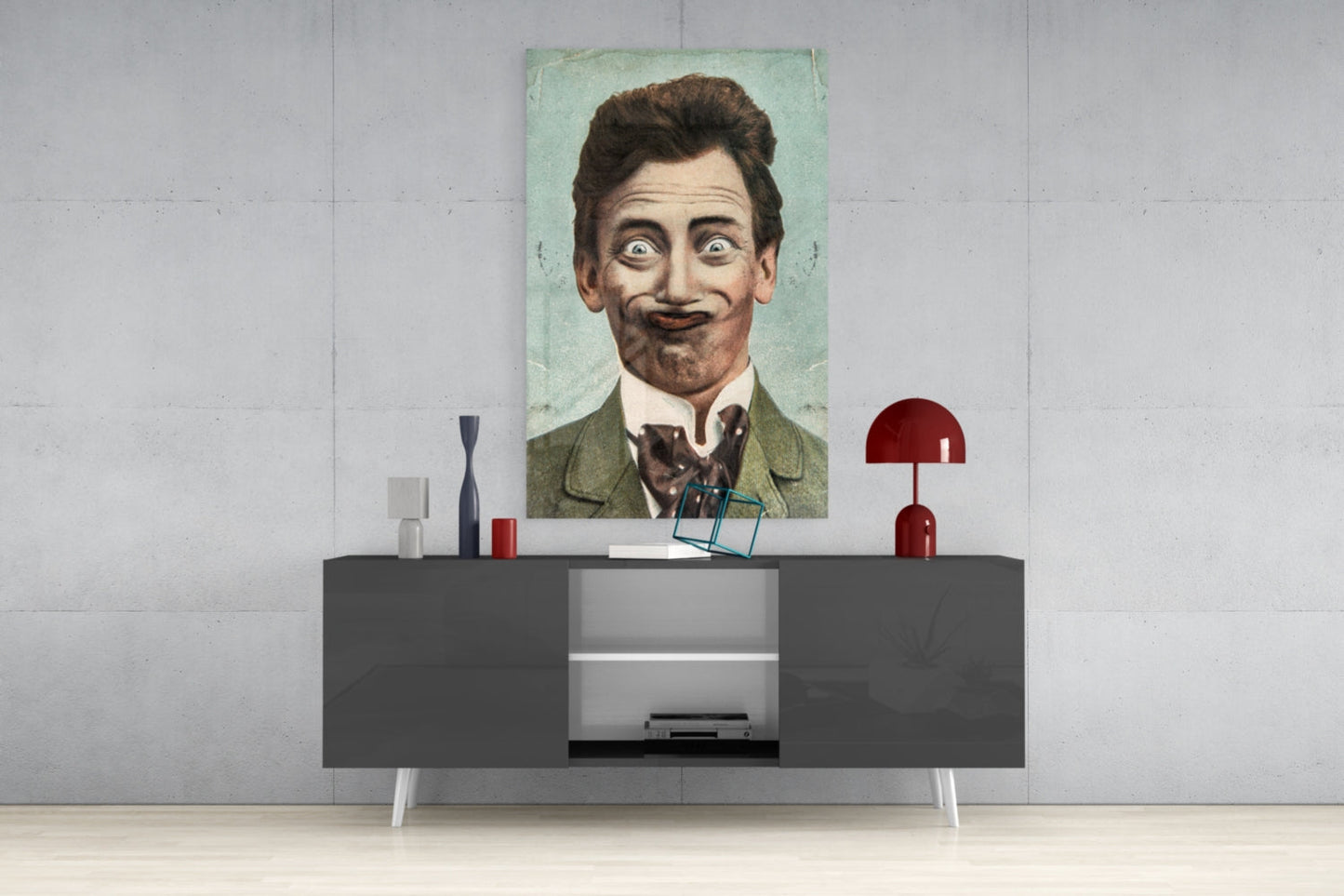Vintage portrait of a mustachioed gentleman in green jacket displayed on white wall above modern gray console table with red lamp and decorative objects.