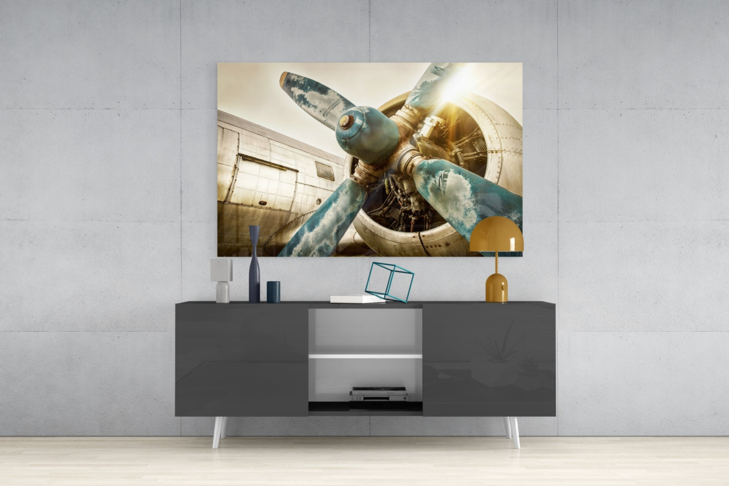 Vintage airplane propeller glass wall art displaying weathered blue and gold tones, mounted above gray media console in modern interior setting.
