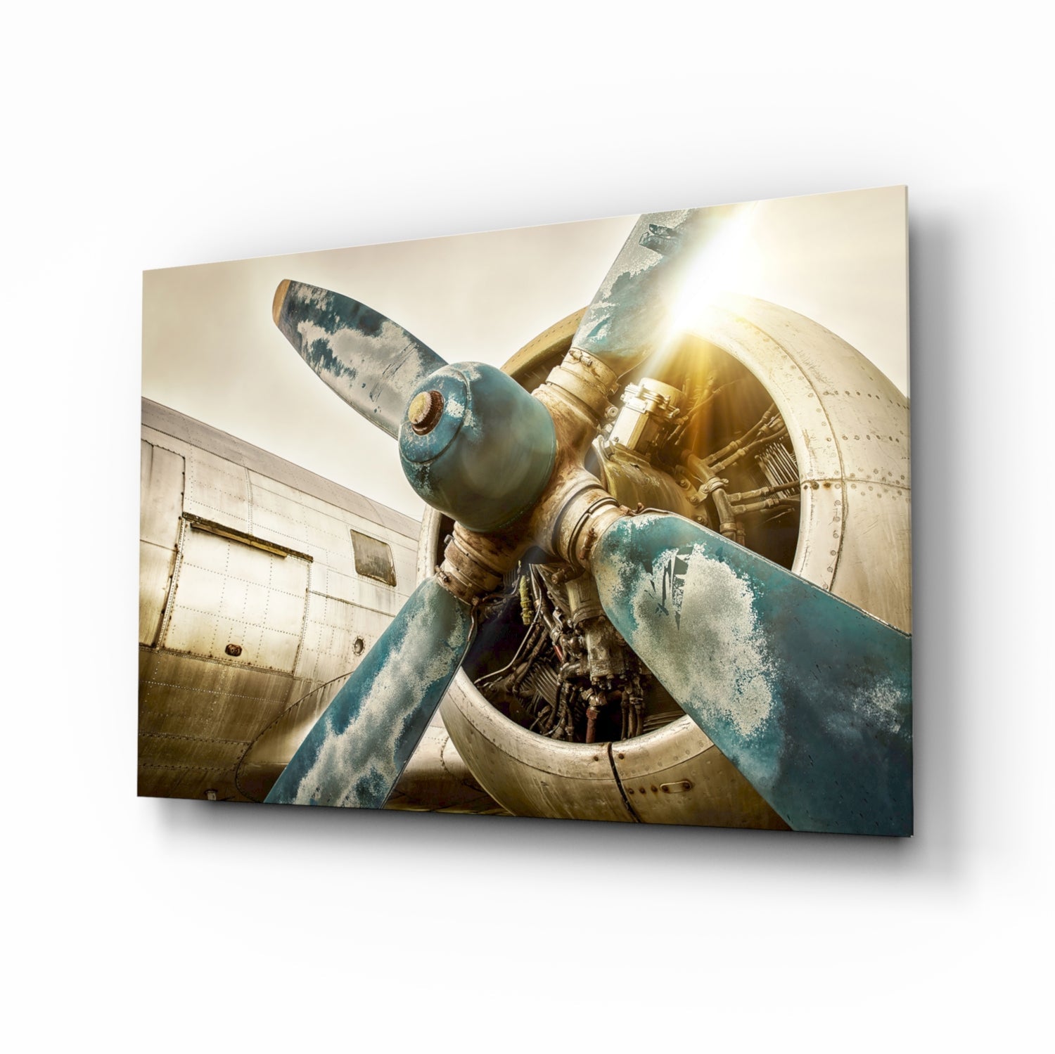 Close-up of a weathered aircraft propeller with blue-green patina and brass hub against a cream-colored fuselage, backlit by golden sunlight.
