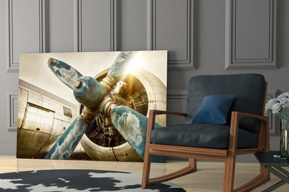 Close-up of vintage aircraft propeller and engine with weathered blue-green metal against warm golden light, displayed as glass wall art in modern interior.