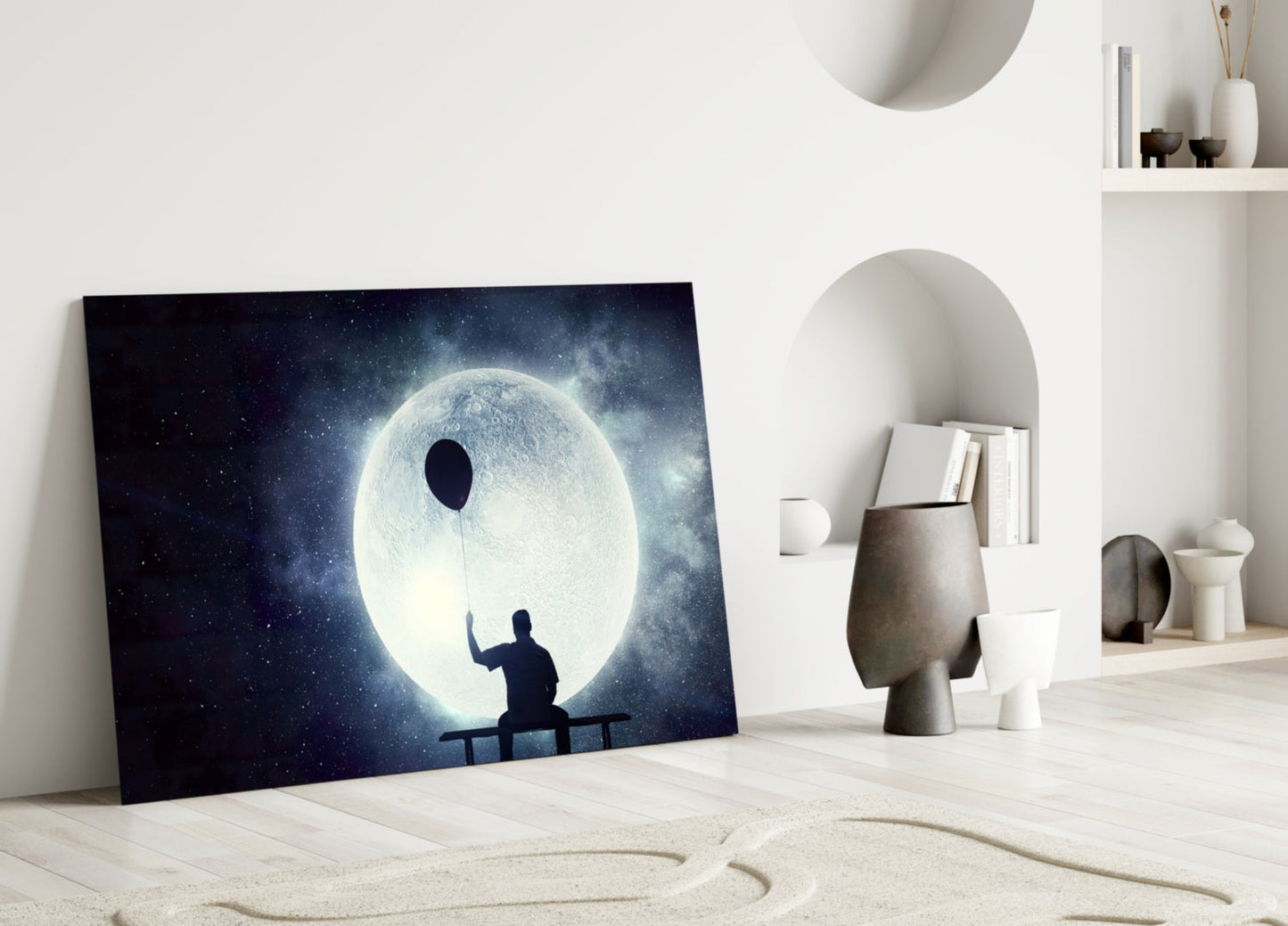 Glass wall art leaning against white wall displays silhouetted figure on bench holding glowing white moon against starry night sky.