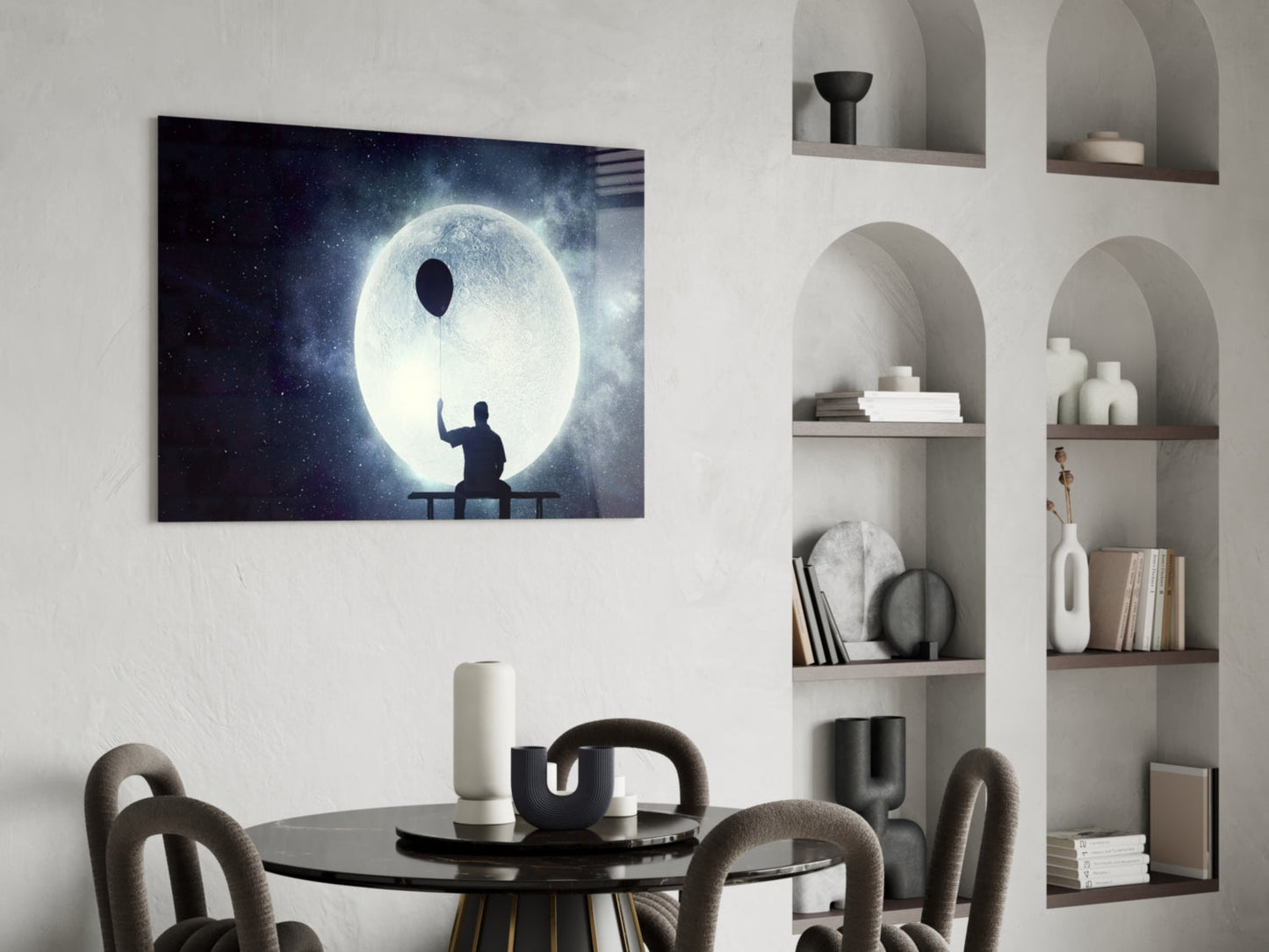 Glass wall art depicting silhouetted figure on bench releasing balloon against glowing moon and starry night sky, displayed above black dining table.