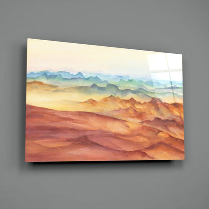 Watercolor mountain landscape painting on glass mounted on gray wall, displaying layered peaks in warm orange, gold, and cool blue tones.