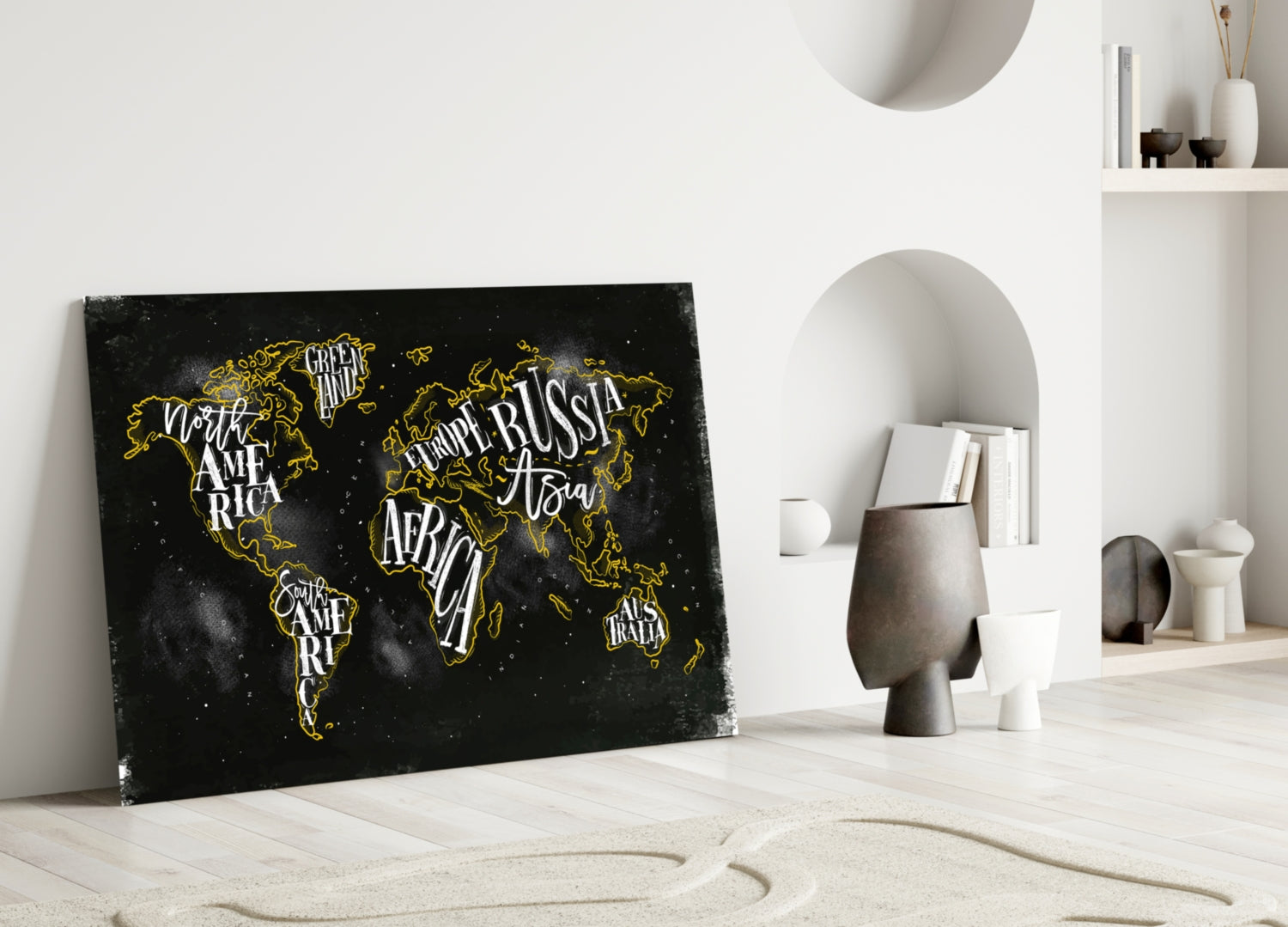 Black canvas world map with gold lettering and outlines leaning against white wall in minimalist room setting.