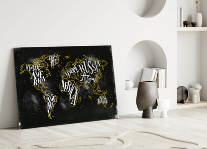 Black canvas world map with gold lettering and outlines leaning against white wall in minimalist room setting.