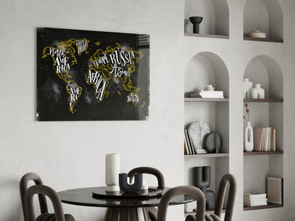 Black world map canvas with gold lettering displayed above round dining table in minimalist interior.