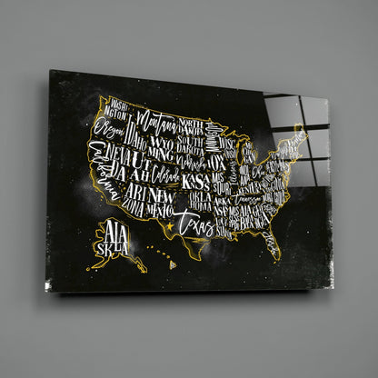 Black glass wall art featuring a gold-outlined USA map with white state names on dark background, angled view showing reflection.