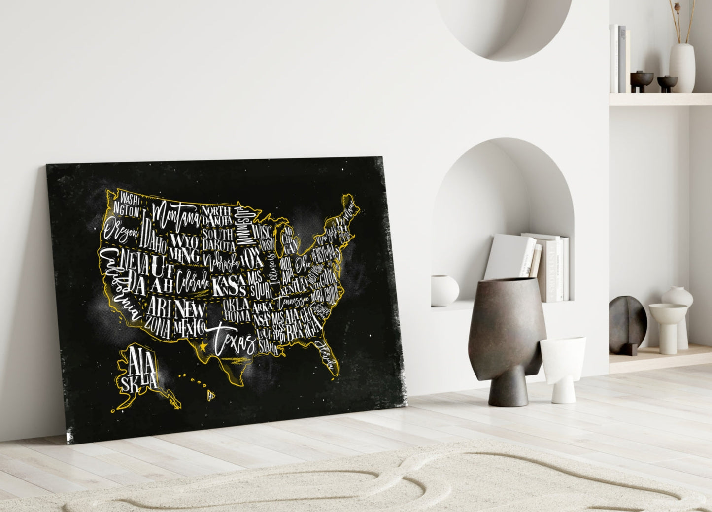 Black glass USA map with gold state names and border leaning against white wall beside decorative objects.