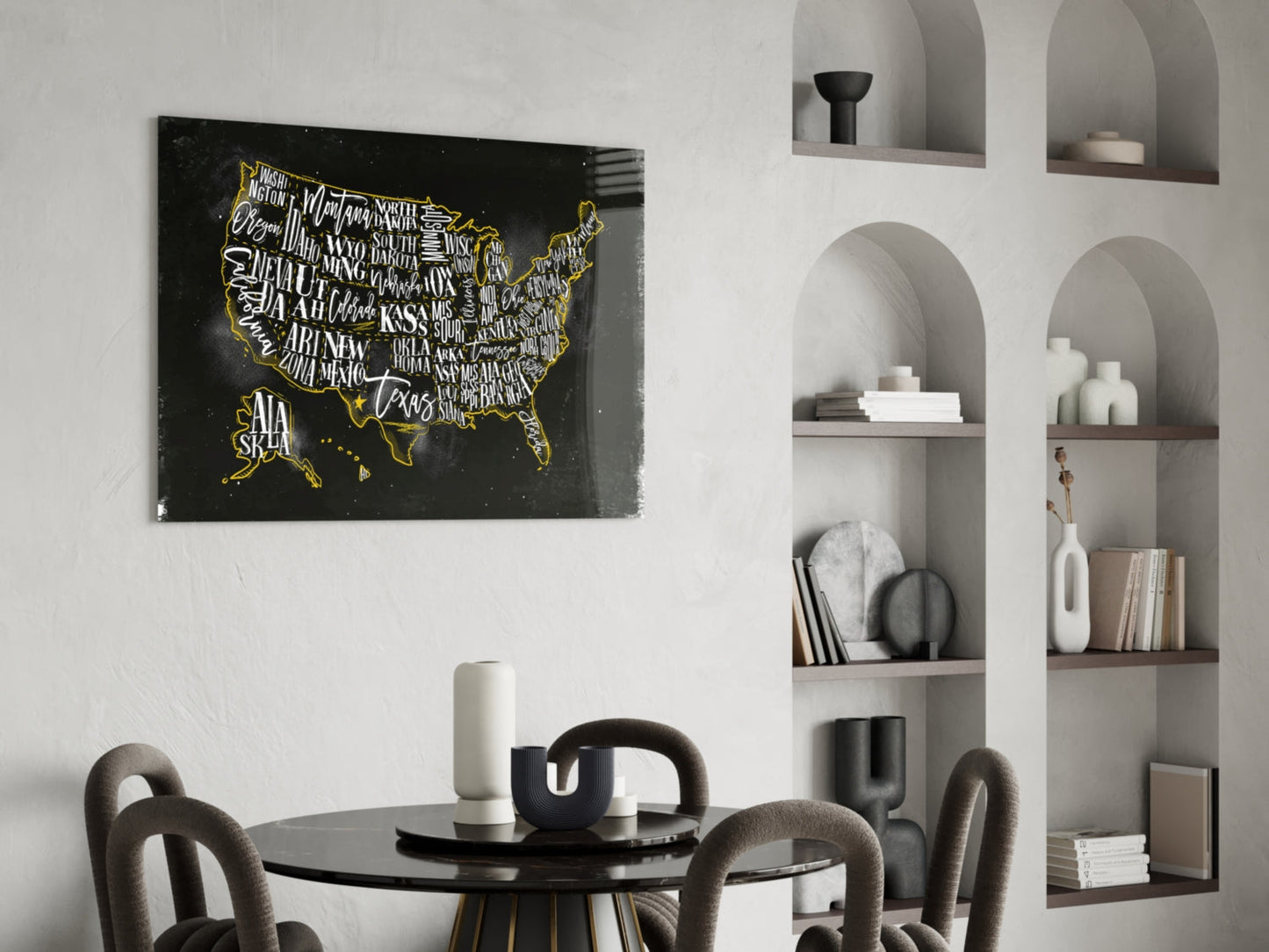 Black glass USA map with gold state names and borders displayed above round dining table in modern interior with white built-in shelving.