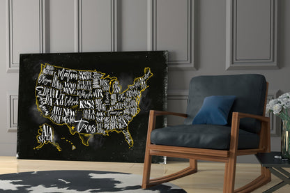 Black glass USA map with gold lettering and border displayed in modern living room next to wooden chair.