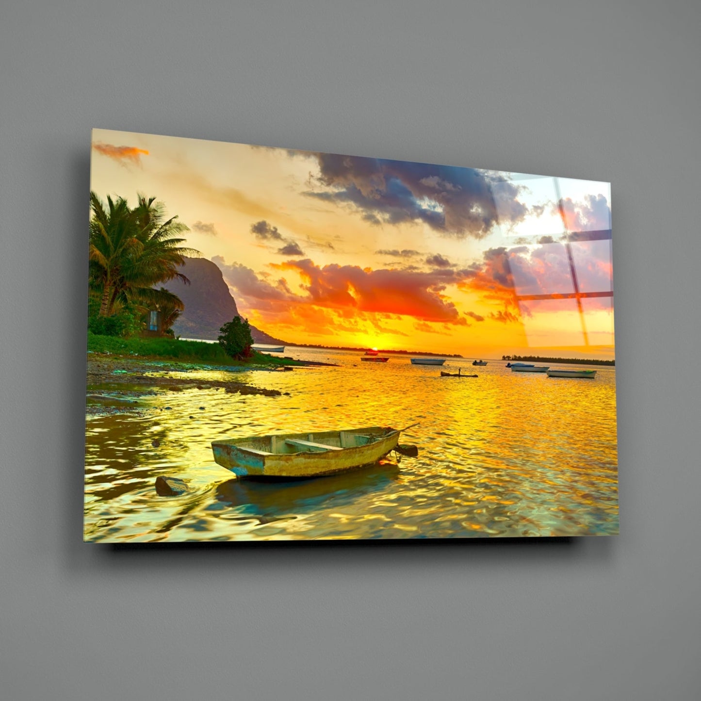 Weathered fishing boat in shallow golden water at sunset with palm trees and mountains under dramatic orange sky.