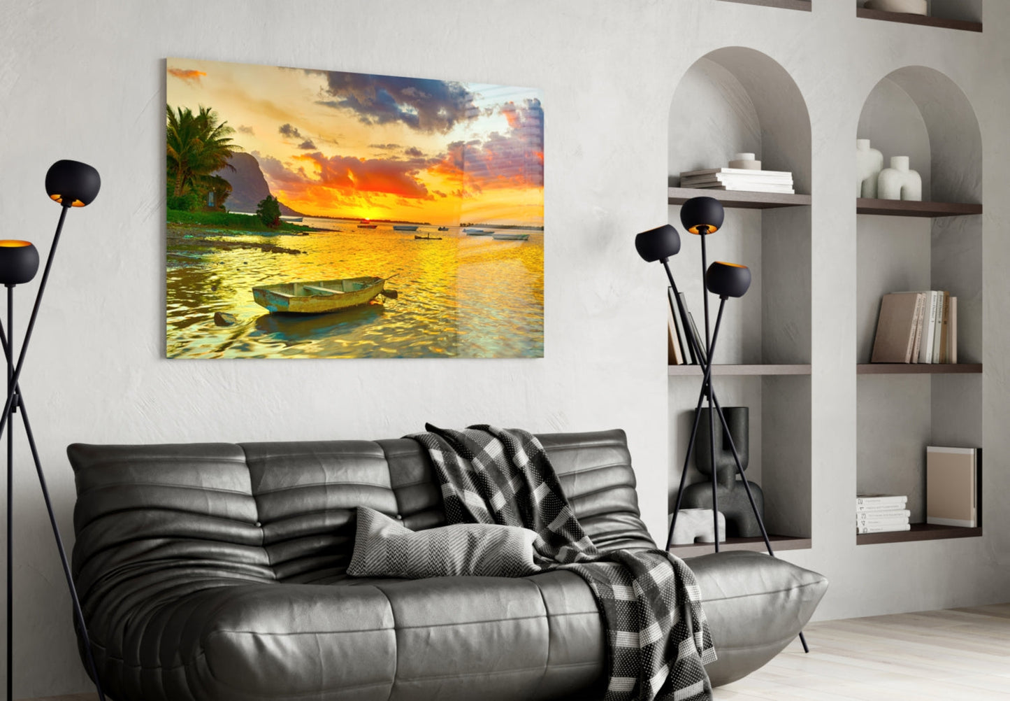 Horizontal canvas print showing golden sunset over tropical bay with moored fishing boat, displayed above black leather sofa in modern living room.