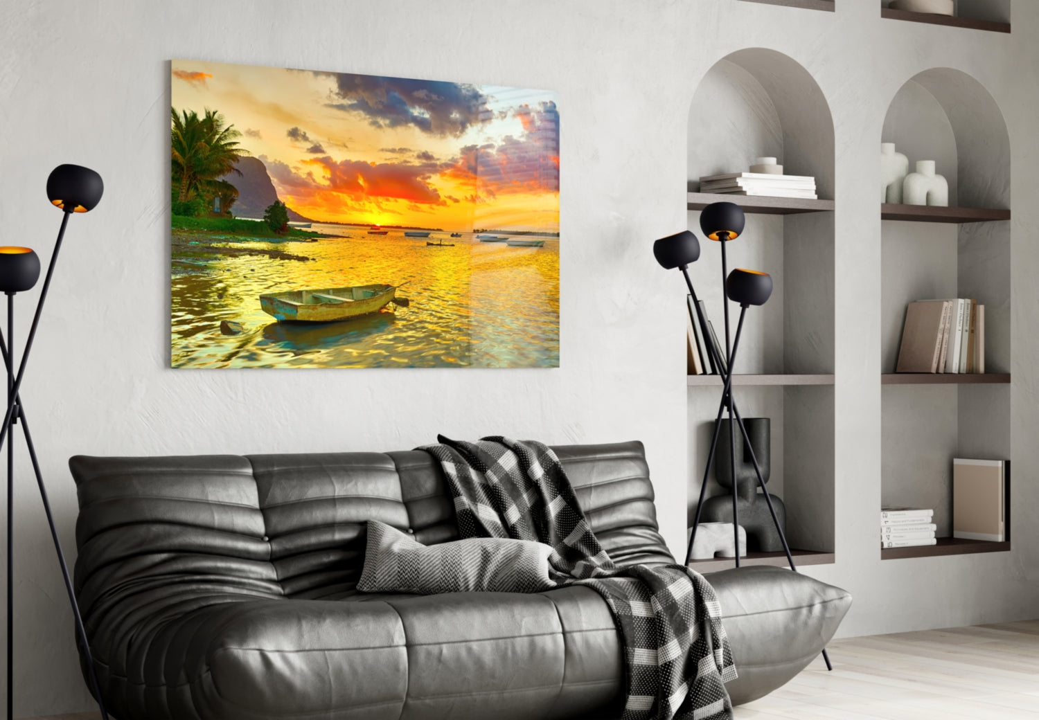 Horizontal canvas print showing golden sunset over tropical bay with moored fishing boat, displayed above black leather sofa in modern living room.