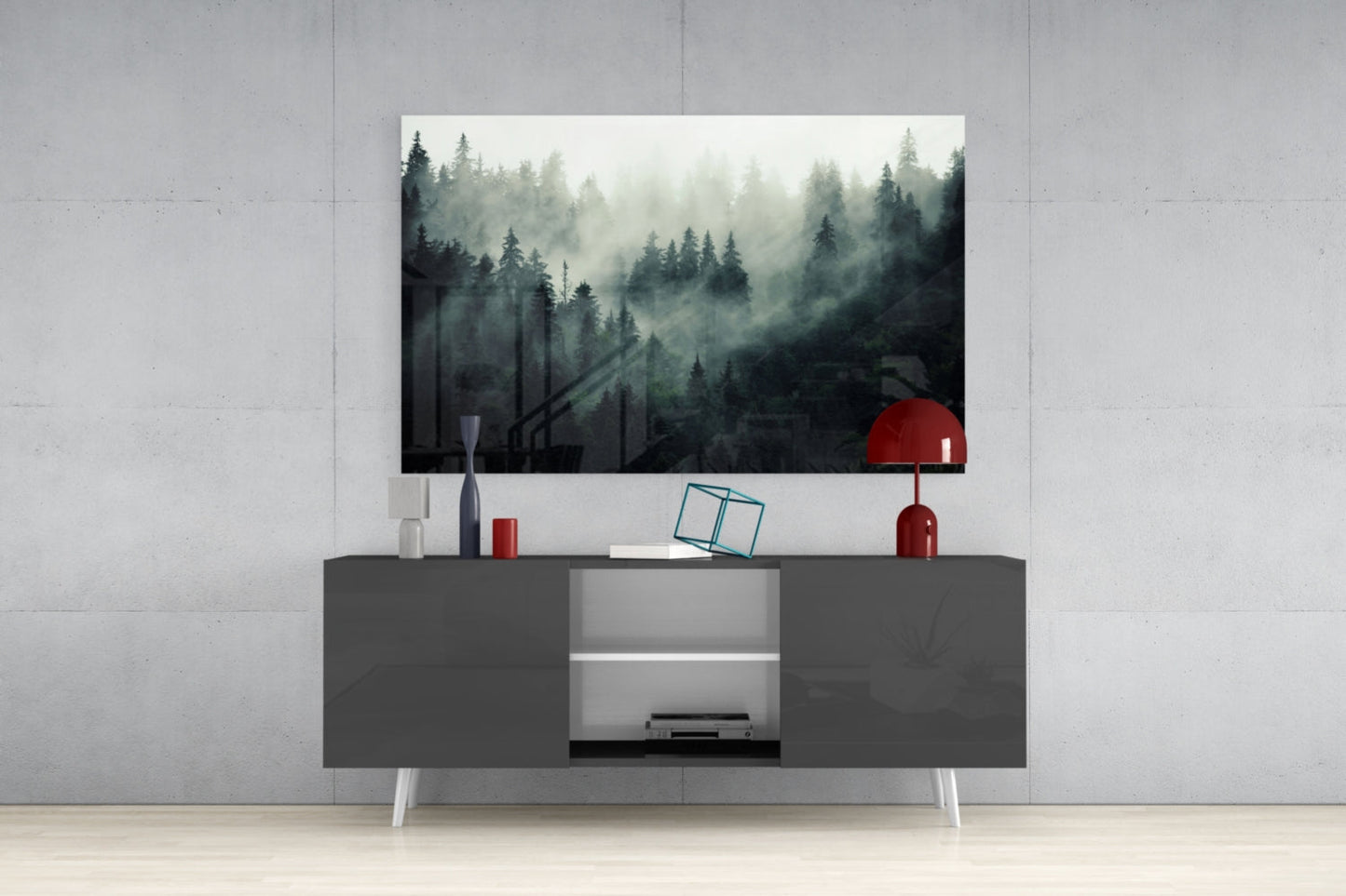 Misty forest glass wall art in greens and grays displayed above a dark gray media console with white legs and red decorative accessories.