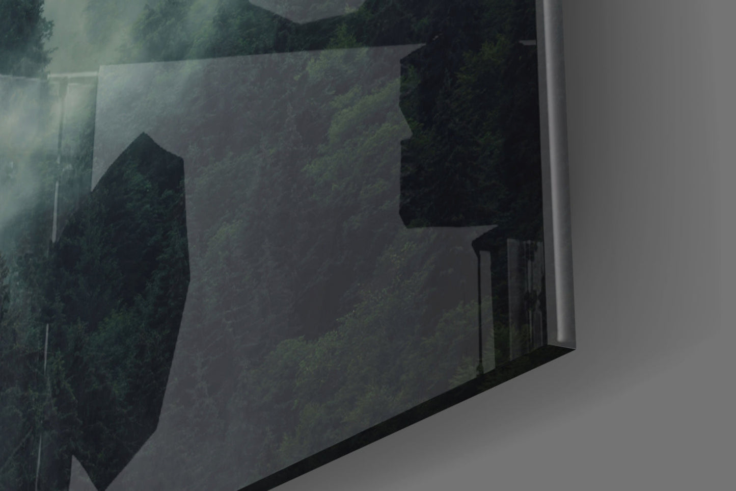 Angled perspective of translucent glass wall art displaying dark forest trees and misty landscape in muted greens and blacks.