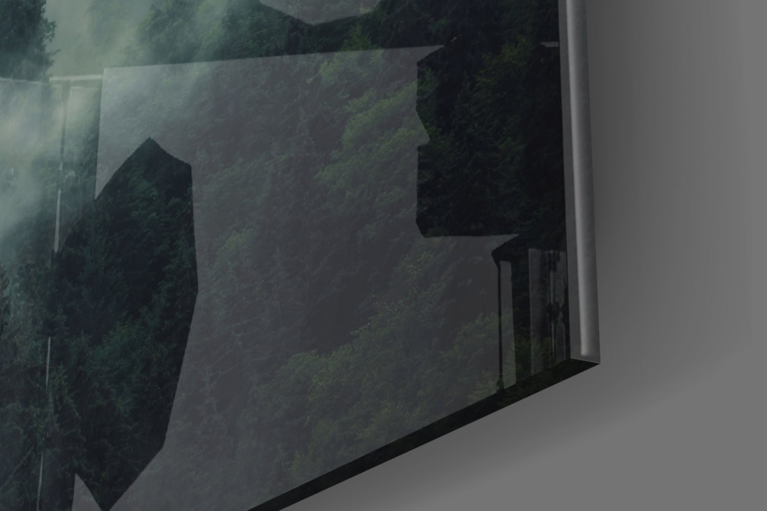 Angled perspective of translucent glass wall art displaying dark forest trees and misty landscape in muted greens and blacks.