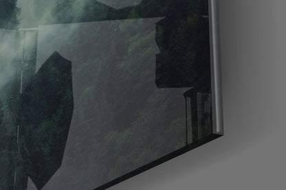Angled perspective of translucent glass wall art displaying dark forest trees and misty landscape in muted greens and blacks.