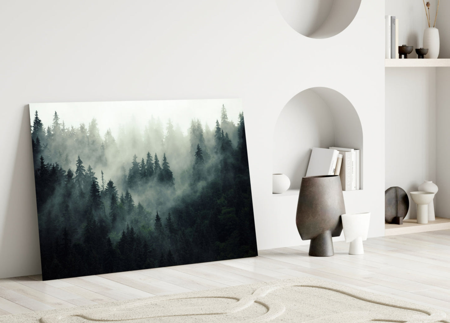 Misty forest glass art leans against white wall in minimalist room with sand floor and ceramic decor.