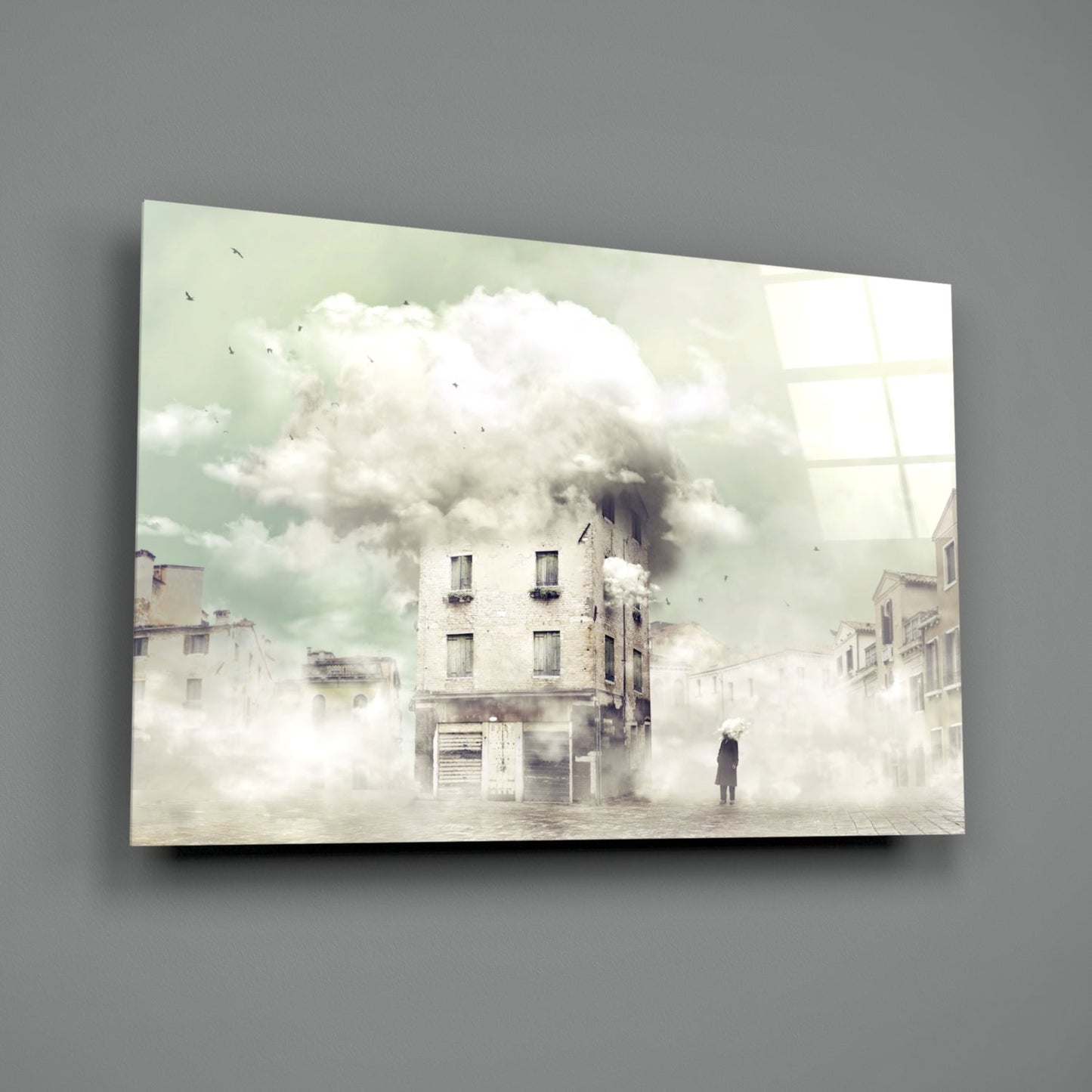 Mounted glass wall art depicting a surreal cityscape with a burning building surrounded by white clouds and a solitary figure standing in fog.