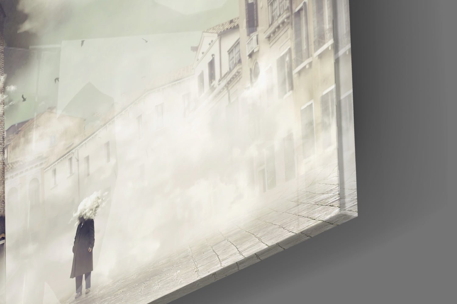 Fog Glass Wall Art mounted on gray wall displaying a solitary figure in dark coat standing in misty European street with pale buildings.