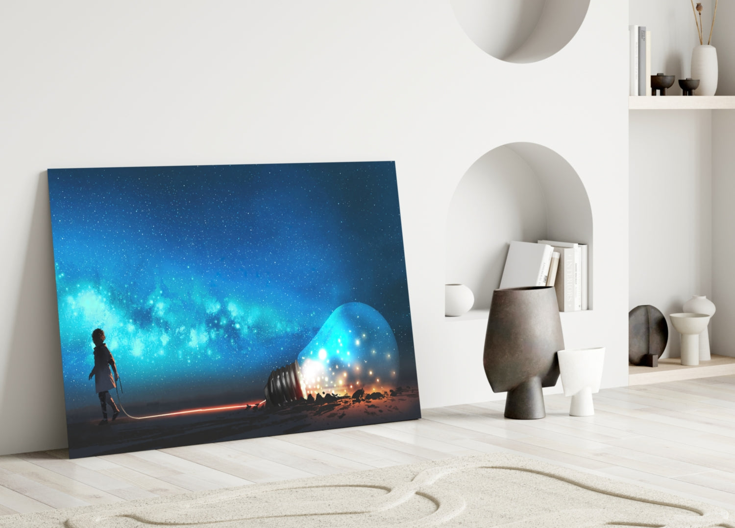 Glass wall art depicting a silhouetted figure holding a glowing blue orb beneath a starry night sky, leaning against a light wood floor beside white decorative objects.