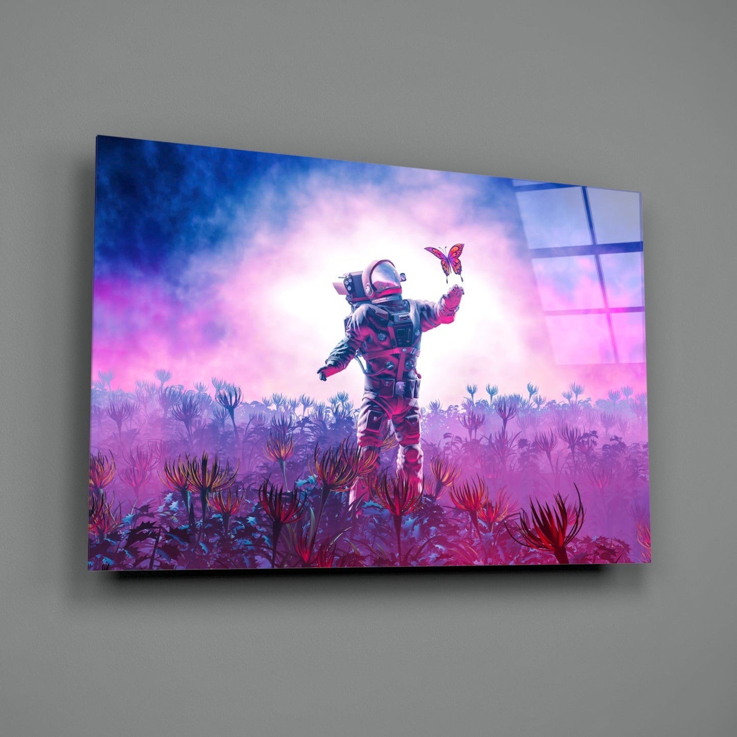 Angled front view of glass wall art displaying an astronaut in a pink and purple alien landscape catching a butterfly, mounted on gray wall.