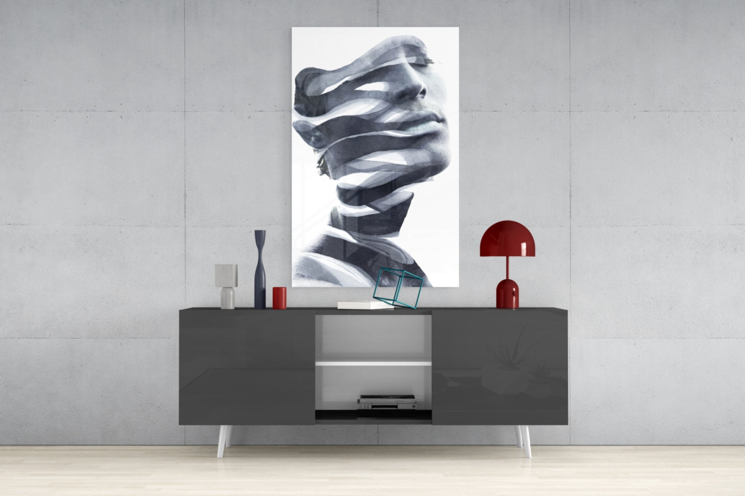 Black and white portrait glass wall art depicting a face with draped fabric, displayed above a dark console table with red lamp and decorative objects.