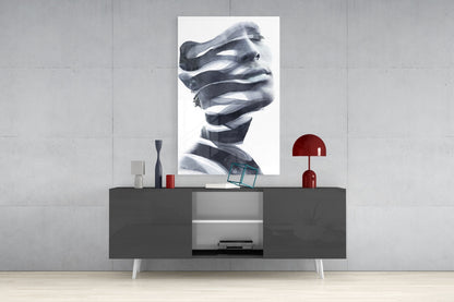 Black and white portrait glass wall art depicting a face with draped fabric, displayed above a dark console table with red lamp and decorative objects.