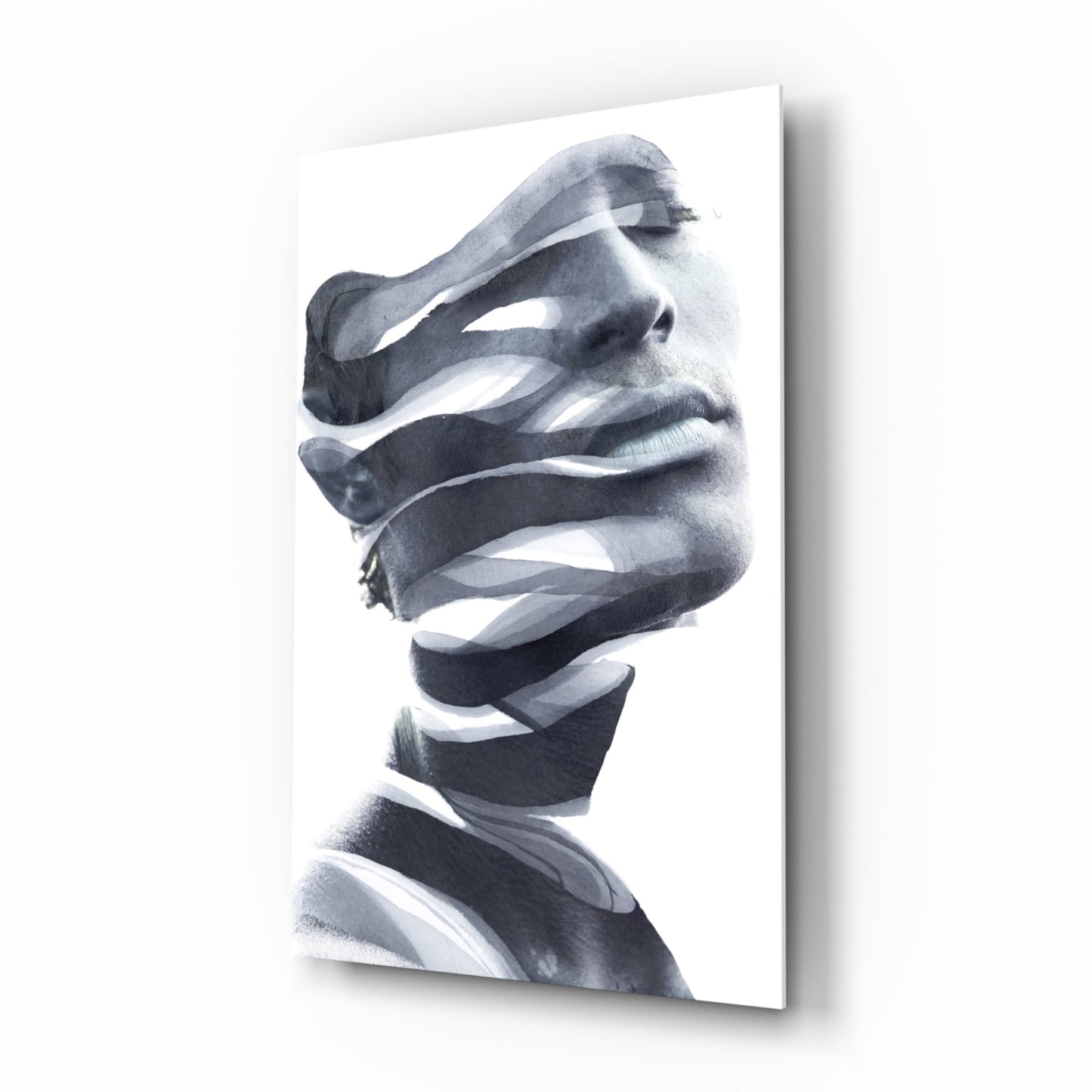 Monochrome glass wall art featuring a man's face in profile with abstract white ribbon-like strips obscuring his features, mounted at an angle.
