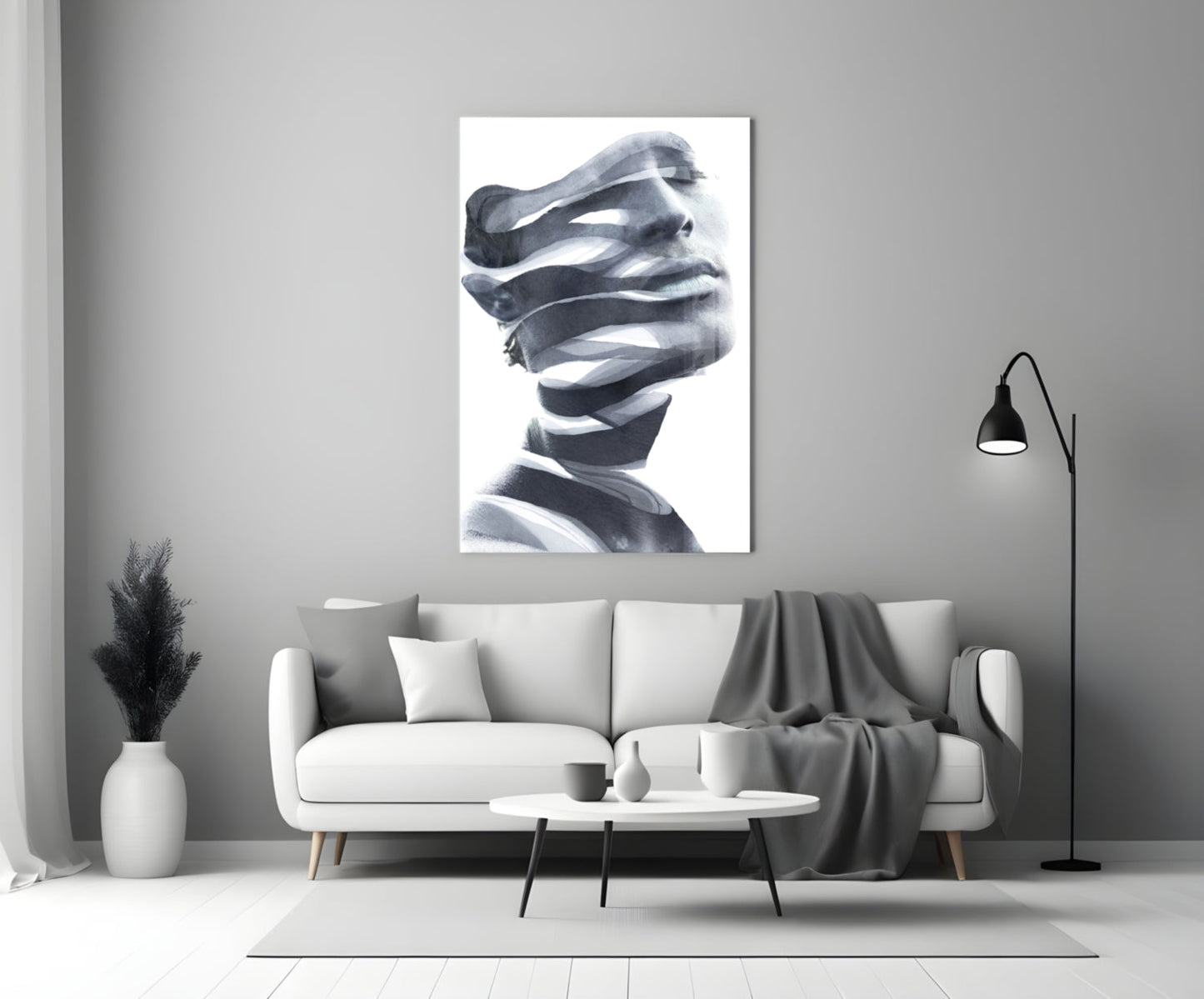 Black and white glass wall art depicting a stylized male head wrapped in translating ribbons, displayed above a gray sofa in a modern living room setting.