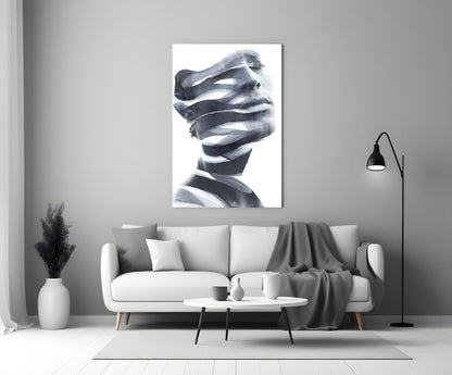 Black and white glass wall art depicting a stylized male head wrapped in translating ribbons, displayed above a gray sofa in a modern living room setting.